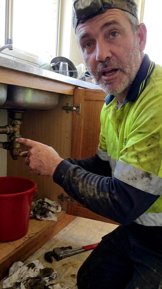 A plumber talking to camera under a sink